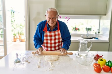 Senior man smiling confident keading dough at kitchen