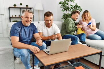 Obraz premium Group of middle age friends smiling happy using smartphone and laptop sitting on the sofa at home.