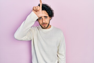 Handsome hispanic man wearing casual white sweater making fun of people with fingers on forehead...