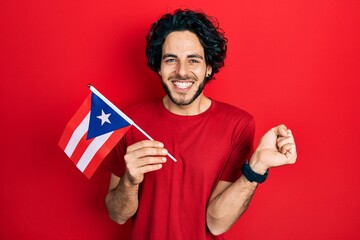 Handsome hispanic man holding puerto rico flag screaming proud, celebrating victory and success...