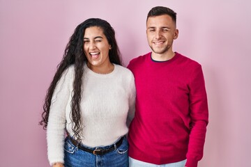 Obraz premium Young hispanic couple standing over pink background winking looking at the camera with sexy expression, cheerful and happy face.