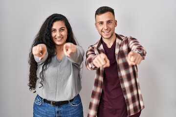 Young hispanic couple standing over white background pointing to you and the camera with fingers, smiling positive and cheerful