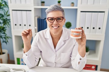 Middle age woman wearing dentist uniform holding brackets and aligner at clinic