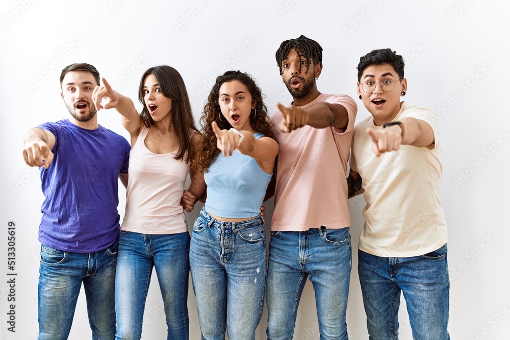 Poster Group of young people standing together over isolated background pointing with finger surprised ahead, open mouth amazed expression, something on the front