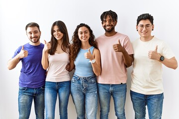 Group of young people standing together over isolated background doing happy thumbs up gesture with...