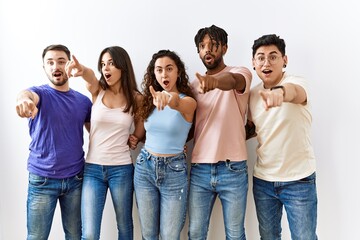Group of young people standing together over isolated background pointing with finger surprised ahead, open mouth amazed expression, something on the front