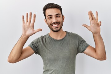 Fototapeta premium Young hispanic man with beard wearing casual t shirt over white background showing and pointing up with fingers number nine while smiling confident and happy.