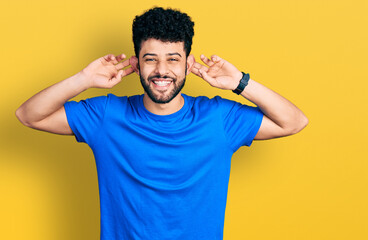 Young arab man with beard wearing casual blue t shirt smiling pulling ears with fingers, funny...