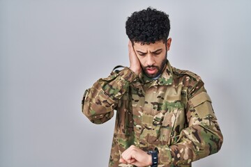 Arab man wearing camouflage army uniform looking at the watch time worried, afraid of getting late