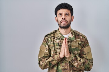 Arab man wearing camouflage army uniform begging and praying with hands together with hope...