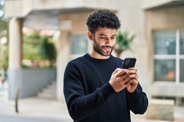 Young arab man smiling confident using smartphone at street