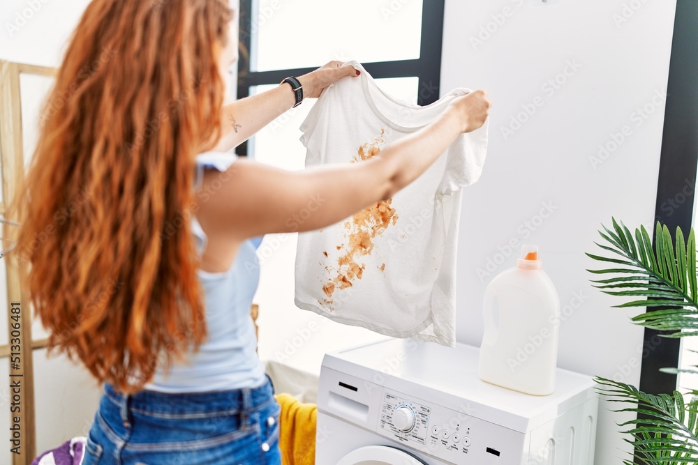 Wall mural young redhead woman holding dirty t shirt at laundry room - Wall murals