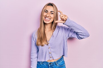 Beautiful hispanic woman wearing casual shirt smiling and confident gesturing with hand doing small size sign with fingers looking and the camera. measure concept.