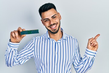 Young hispanic man with beard holding memory ram smiling happy pointing with hand and finger to the...