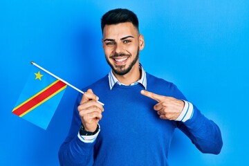 Young hispanic man with beard holding democratic republic of the congo flag smiling happy pointing with hand and finger