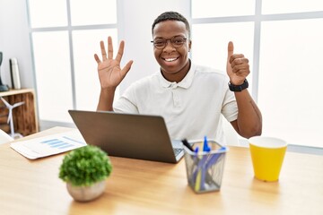 Young african man working at the office using computer laptop showing and pointing up with fingers number six while smiling confident and happy.