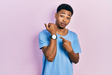 Young african american man wearing casual blue t shirt in hurry pointing to watch time, impatience,...