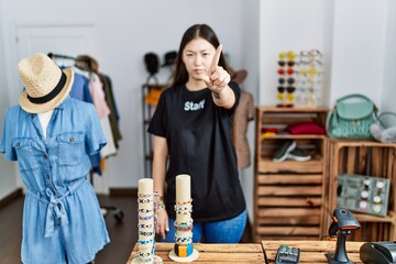 Young asian woman working as manager at retail boutique pointing with finger up and angry expression, showing no gesture