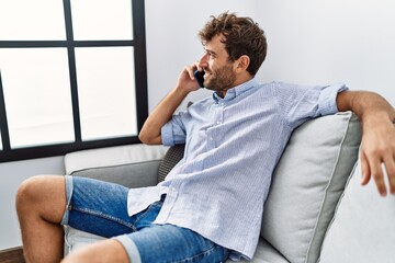 Young hispanic man talking on the smartphone sitting on the sofa at home.