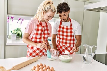 Young couple smiling happy mixing ingredients to make dough for homemade bread at kitchen.