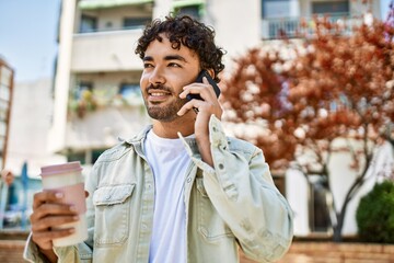 Handsome hispanic man with beard smiling happy outdoors on a sunny day having a conversation...
