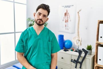 Young man with beard working at pain recovery clinic relaxed with serious expression on face. simple and natural looking at the camera.