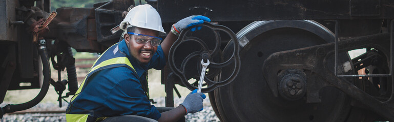 African machine engineer technician wearing a helmet, groves and safety vest is using a wrench to...
