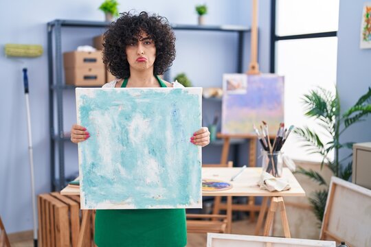 Young brunette woman with curly hair holding painter canvas depressed and worry for distress, crying angry and afraid. sad expression.