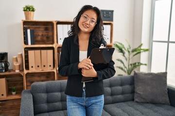 Young chinese woman psychologist holding clipboard standing at clinic