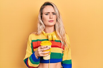 Obraz premium Beautiful young blonde woman drinking cup of coffee wearing headphones skeptic and nervous, frowning upset because of problem. negative person.