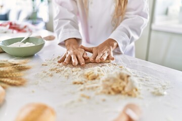 Obraz na płótnie Canvas Young woman wearing cook uniform kneading dough at kitchen
