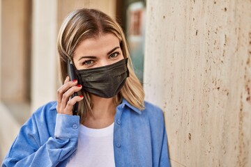 Young blonde girl wearing coronavirus mask talking on the smartphone at the city.
