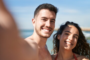 Fototapeta premium Young hispanic couple tourists wearing swimsuit make selfie by camera at seaside