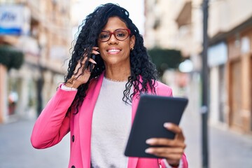 Fototapeta premium African american woman executive talking on the smartphone holding touchpad at street