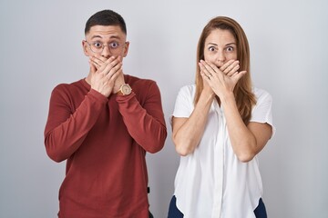 Mother and son standing together over isolated background shocked covering mouth with hands for...