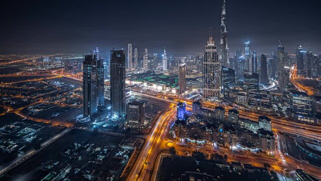 Panorama showing aerial view of tallest towers in Dubai Downtown skyline and highway night timelapse panorama. Financial district and business area in smart urban city. Skyscraper and high-rise