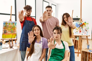 Group of five hispanic artists at art studio doing stop sing with palm of the hand. warning expression with negative and serious gesture on the face.