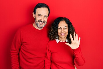 Fototapeta premium Middle age couple of hispanic woman and man hugging and standing together showing and pointing up with fingers number five while smiling confident and happy.