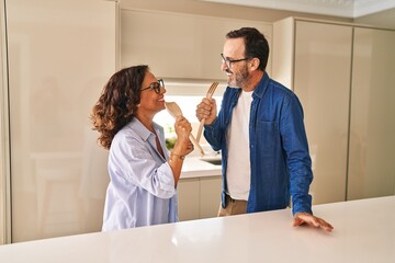 Middle age hispanic couple smiling confident singing song at kitchen
