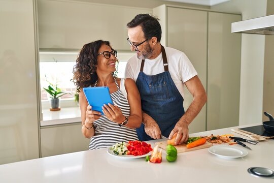 Middle age hispanic couple smiling confident cooking and using touchpad at kitchen