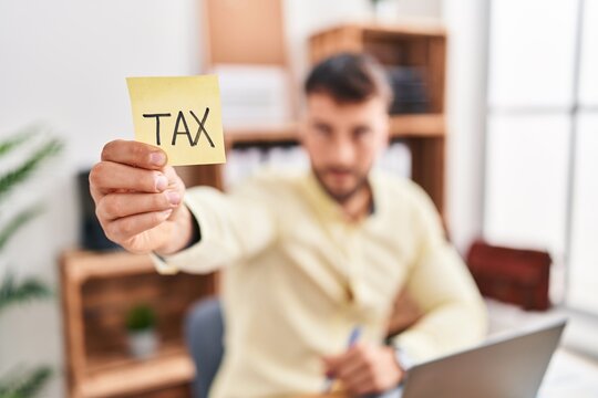 Young hispanic man business worker holding tax reminder paper at office