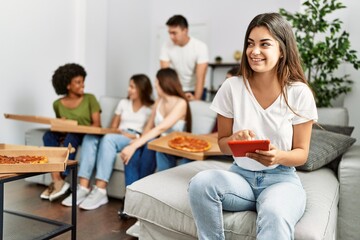 Group of young friends eating italian sitting on the sofa. Woman smiling and using touchpad at home.