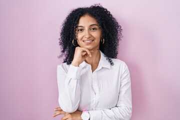 Fototapeta na wymiar Hispanic woman with curly hair standing over pink background with hand on chin thinking about question, pensive expression. smiling and thoughtful face. doubt concept.