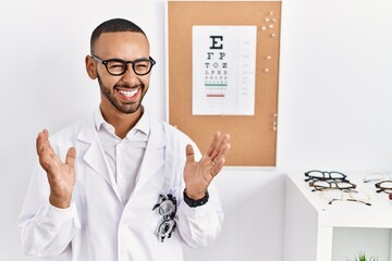 African american optician man standing by eyesight test celebrating mad and crazy for success with...