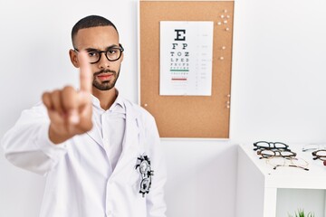 Fototapeta na wymiar African american optician man standing by eyesight test pointing with finger up and angry expression, showing no gesture