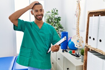 Fototapeta premium African american physiotherapist man working at pain recovery clinic smiling confident touching hair with hand up gesture, posing attractive and fashionable