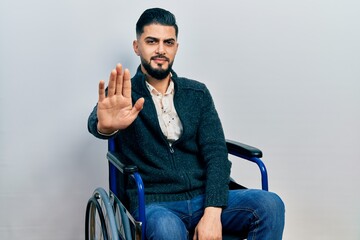 Handsome man with beard sitting on wheelchair doing stop sing with palm of the hand. warning expression with negative and serious gesture on the face.