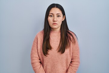 Young latin woman standing over blue background relaxed with serious expression on face. simple and natural looking at the camera.