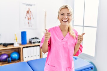 Young caucasian woman working at pain recovery clinic success sign doing positive gesture with hand, thumbs up smiling and happy. cheerful expression and winner gesture.