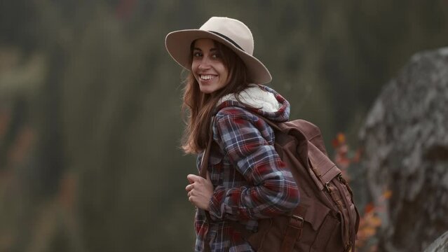 portrait of joyful young female hiker in hat standing on cliff on forest background and looking with smile, mountain view, travel and sports. touristic places in Ukraine, Tustan National Park.